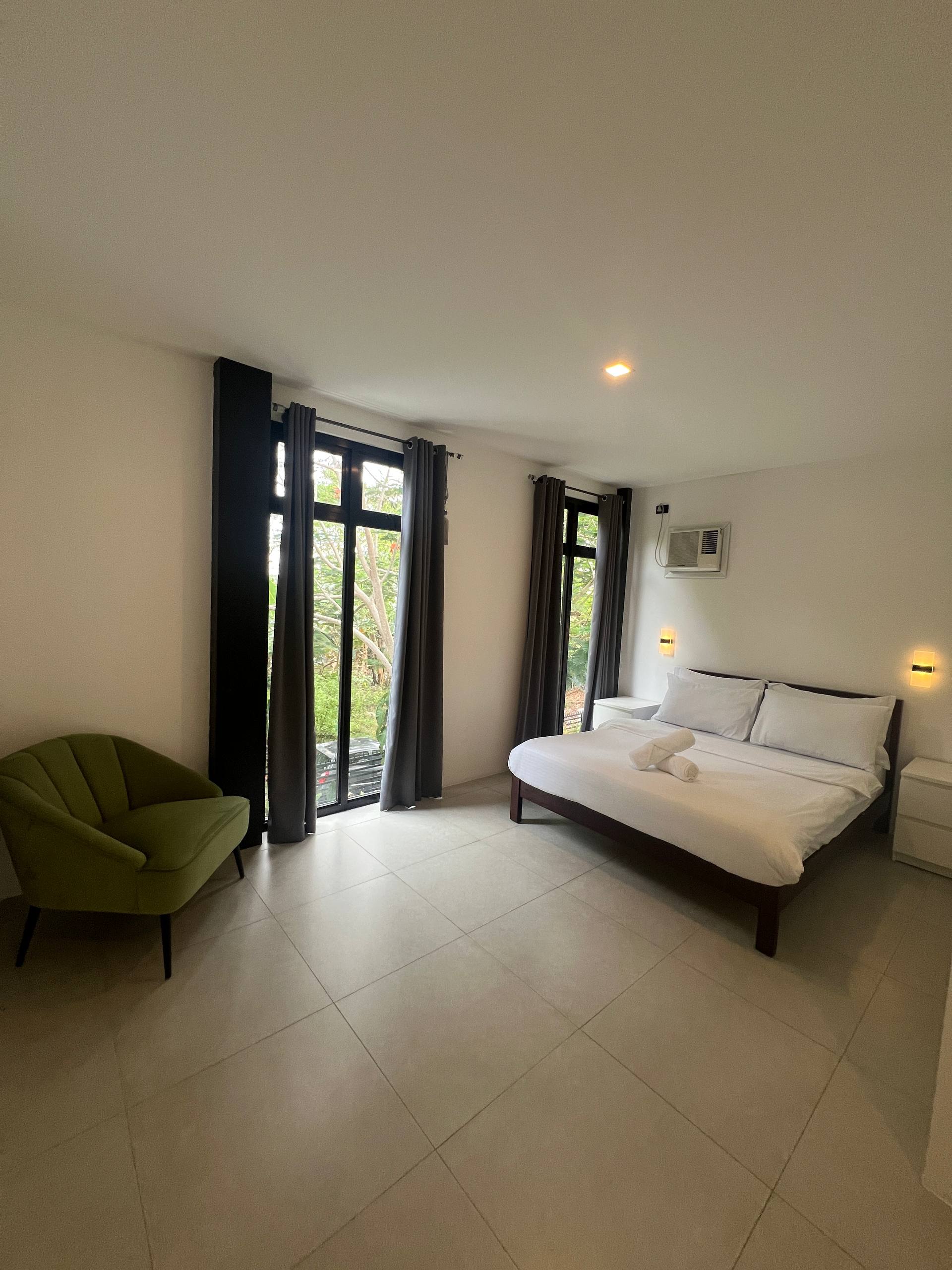 Bedroom 2 with lime-green armchair and garden view through glass windows