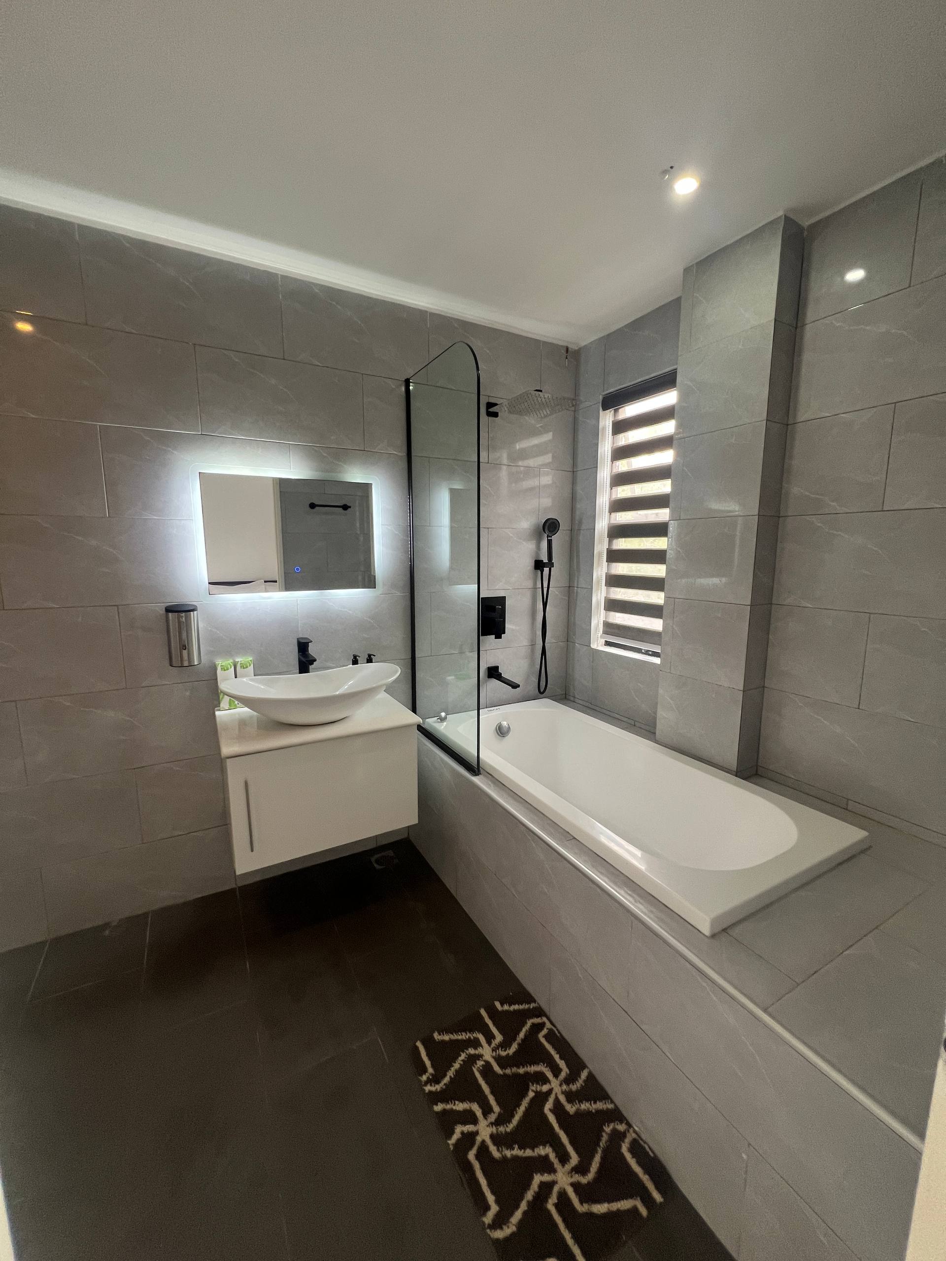 En-suite vanity, mirror and bathtub with glass screen